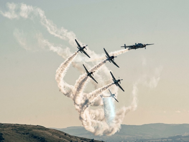 Formation of aircraft trailing smoke loops across a pale sky above hills
