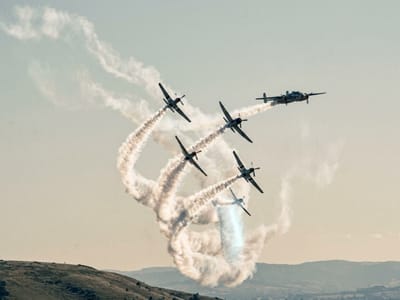 Formation of aircraft trailing smoke loops across a pale sky above hills