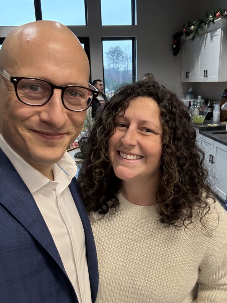Adam Buice and a colleague smiling together at an office Christmas party, holiday garland and a Christmas tree visible in the background