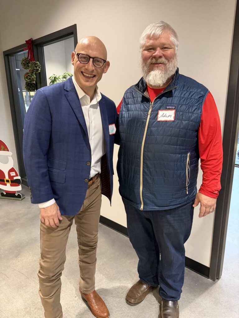 Adam Buice posing with a colleague at a holiday office party, Christmas decorations visible in the background