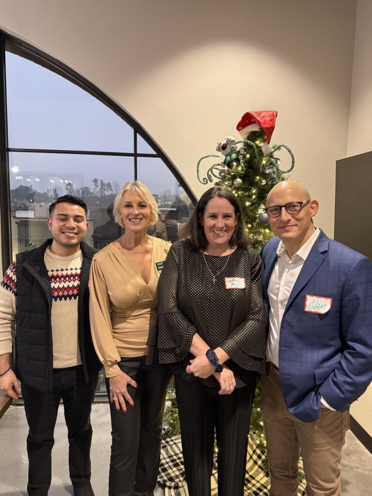 Adam Buice and three colleagues posing in front of a decorated Christmas tree at an office holiday party
